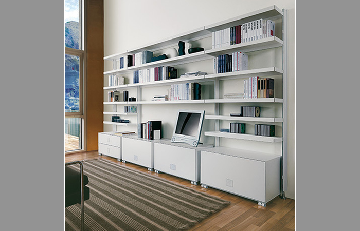 Una moderna libreria bianca con ripiani pieni di libri, una TV al centro e cassetti inferiori, in una stanza luminosa.