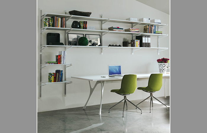 Ufficio moderno con scaffalature minimaliste, tavolo bianco, due sedie verdi e decorazioni varie su una parete bianca.