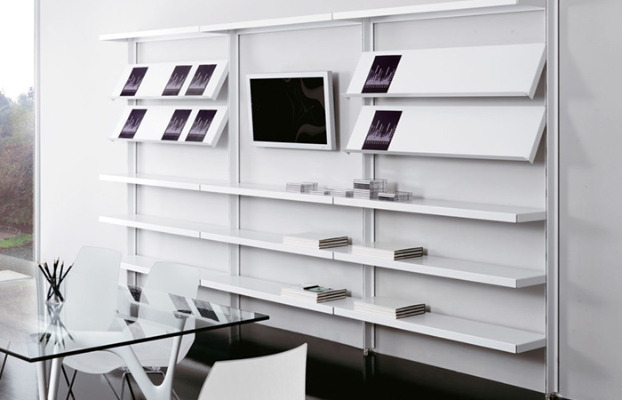 Sala riunioni moderna con scaffali bianchi, libri, una TV a parete e un tavolo con sedie trasparenti.